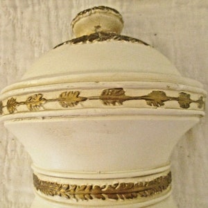 May include: White ceramic bottle stopper with gold leaf accents. The bottle stopper has a round top and a cylindrical base.