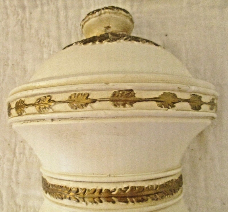 May include: White ceramic bottle stopper with gold leaf accents. The bottle stopper has a round top and a cylindrical base.