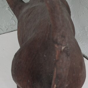 May include: A brown, wooden monkey sculpture with a long tail. The monkey is standing on all fours and its head is turned to the side.