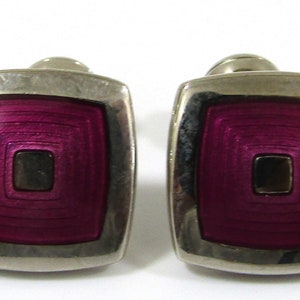 May include: A pair of silver cufflinks with a square, concentric circle design in a deep purple color.