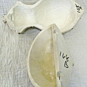 May include: Two white plaster molds, one shaped like a pear and the other shaped like a half-circle. The pear mold has a small knob on the top and the number "168" written on the side. The half-circle mold has the number "168" written on the side.