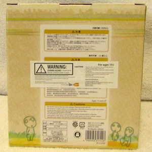 May include: A cardboard box with a warning label for ages 15 and up. The box features a cartoon character with a large head and small body. The text on the box reads "Studio Ghibli".