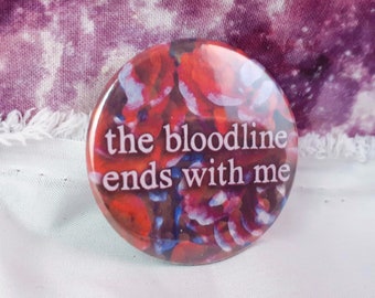 Puede incluir: Botón redondo con un diseño floral en rojo, blanco y azul, con el texto blanco "the bloodline ends with me". El botón está sobre un fondo de tela morada.
