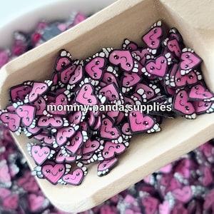 May include: A scoop filled with pink heart-shaped resin charms with black outlines and white eyes and teeth. The charms have a cartoonish, whimsical look.