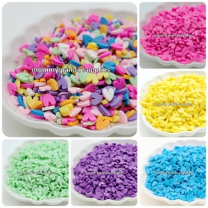 May include: Assortment of colorful heart-shaped sprinkles in six different colors: pink, yellow, green, purple, blue, and multi-colored. The sprinkles are in small bowls and are perfect for decorating cakes, cupcakes, and other desserts.