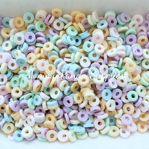 May include: A close-up of a pile of pastel-coloured, ring-shaped beads. The beads are in shades of yellow, green, blue, and purple. The text "Mommy Panda Supplies" is visible.