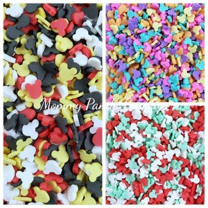 May include: Assortment of colourful Mickey Mouse head shaped sprinkles. The sprinkles are in four different colours: red, yellow, black, and white. The sprinkles are in a square shape.