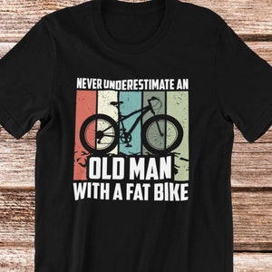 May include: Black t-shirt with a vintage-style graphic of a bicycle and the text "Never underestimate an old man with a fat bike."