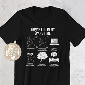 May include: Black t-shirt with white text that reads "Things I do in my spare time". The text is surrounded by illustrations of miniature making activities, including making miniatures, looking at others making miniatures, researching miniatures, talking about miniature making, thinking about miniature making, and dreaming about miniature making.