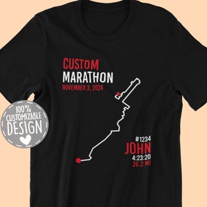 May include: Black t-shirt with a white graphic of a marathon route. The text "CUSTOM MARATHON" is at the top of the graphic, followed by "NOVEMBER 3, 2024". The text "#1234 JOHN 4:23:20 26.2 MI" is at the bottom of the graphic.