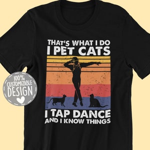 May include: Black t-shirt with a vintage-style graphic design. The design features a silhouette of a person tap dancing with two cats. The text reads "That's what I do I pet cats I tap dance and I know things".