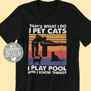 Peut inclure: T-shirt noir avec un design graphique de style vintage. Le texte dit "That's what I do I pet cats I play pool and I know things". Le graphique représente une silhouette d'une personne jouant au billard avec deux chats.