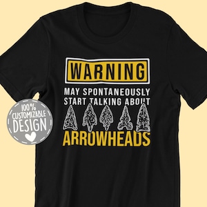 May include: Black t-shirt with a yellow warning sign that says "WARNING MAY SPONTANEOUSLY START TALKING ABOUT ARROWHEADS". There are four arrowhead illustrations below the text.