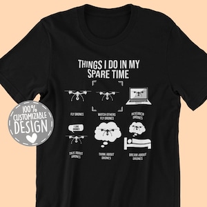 May include: Black t-shirt with white text that reads "Things I do in my spare time". The text is surrounded by a white box. There are six white icons of drones and drone-related activities, including flying drones, watching others fly drones, researching drones, talking about drones, thinking about drones, and dreaming about drones.