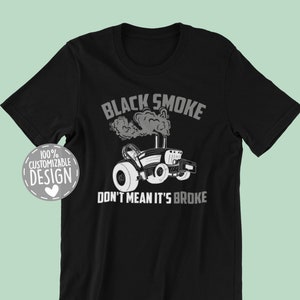 May include: Black t-shirt featuring a tractor graphic with the text "BLACK SMOKE DON'T MEAN IT'S BROKE" in gray and white. The design includes a stylized tractor emitting smoke. A circular design reads "100% CUSTOMIZABLE DESIGN".
