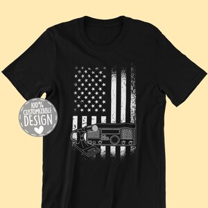 May include: Black t-shirt with a white and gray American flag design. The flag has a radio transceiver in front of it. The text "100% Customizable Design" is in a white circle with a heart in the center.