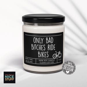 May include: A white soy candle in a glass jar with a black lid. The label reads "ONLY BAD BITCHES RIDE BIKES" with a bicycle graphic. It also states "BURN TIME: 50-60 HRS" and "9 OZ". A sticker says "100% CUSTOMIZABLE DESIGN".