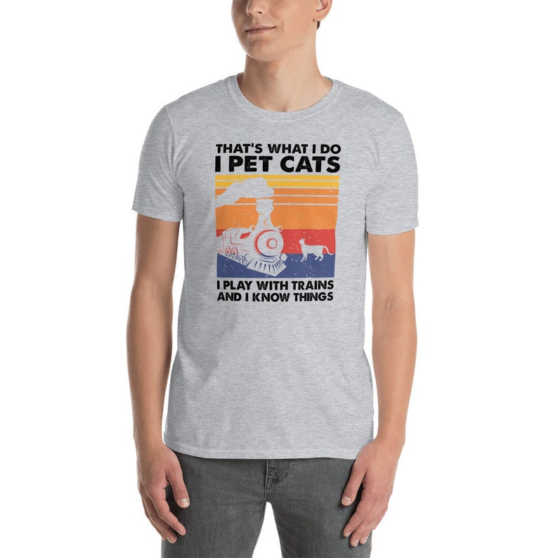 May include: A gray t-shirt with a retro-style graphic of a train and a cat. The text on the shirt reads "That's what I do I pet cats I play with trains and I know things."