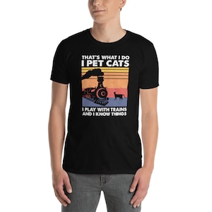 May include: Black t-shirt with a vintage-style graphic of a train and a cat. The text on the shirt reads "That's what I do I pet cats I play with trains and I know things."
