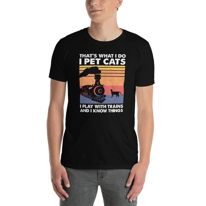 May include: Black t-shirt with a vintage-style graphic of a train and a cat. The text on the shirt reads "That's what I do I pet cats I play with trains and I know things."