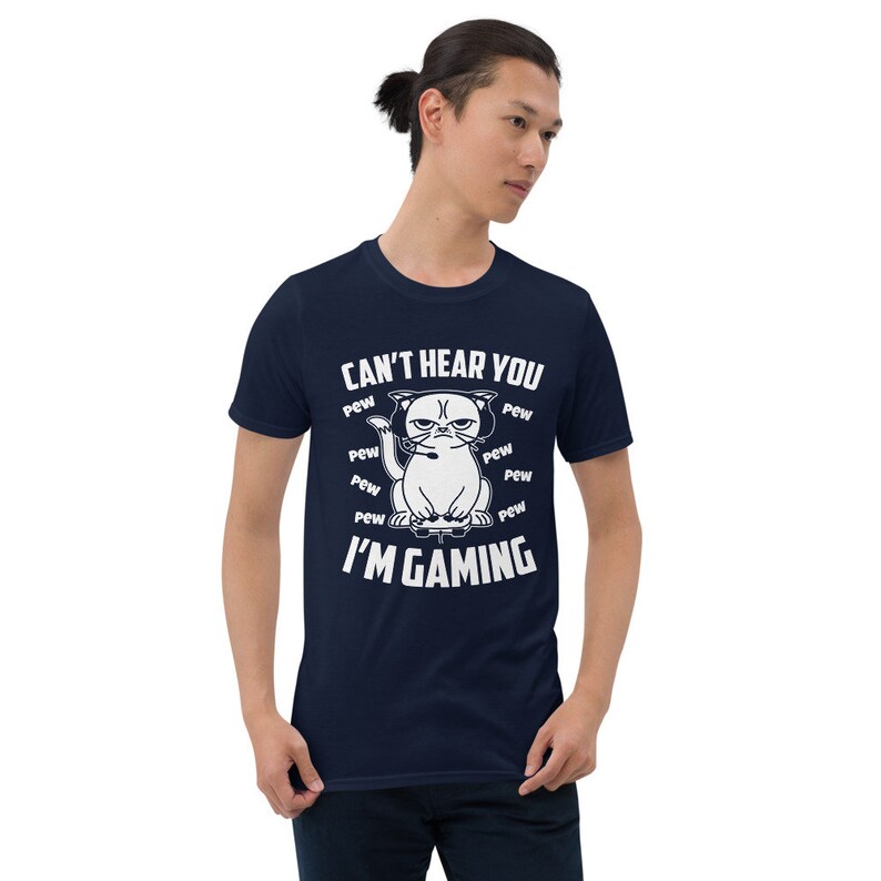 May include: A navy blue t-shirt with a white graphic of a cat wearing headphones and holding a video game controller. The text "Can't hear you I'm gaming" is printed on the shirt, surrounded by the word "pew" repeated multiple times.