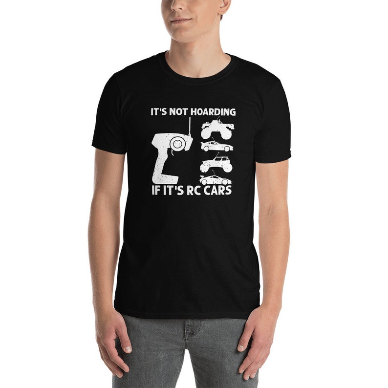 Peut inclure: T-shirt noir avec un motif blanc. Le motif comprend une t&eacute;l&eacute;commande, quatre silhouettes de voitures RC et le texte "IT'S NOT HOARDING IF IT'S RC CARS". Le t-shirt est &agrave; manches courtes et a un col rond.