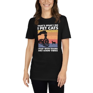 May include: Black t-shirt with a vintage-style graphic of a train and a cat. The text on the shirt reads "That's what I do I pet cats I play with trains and I know things."