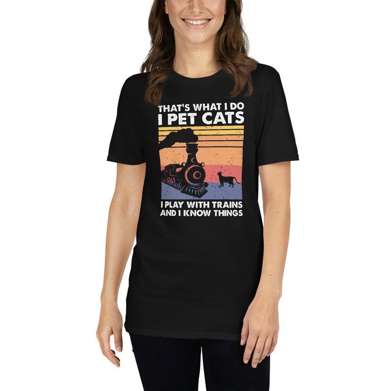 May include: Black t-shirt with a vintage-style graphic of a train and a cat. The text on the shirt reads "That's what I do I pet cats I play with trains and I know things."