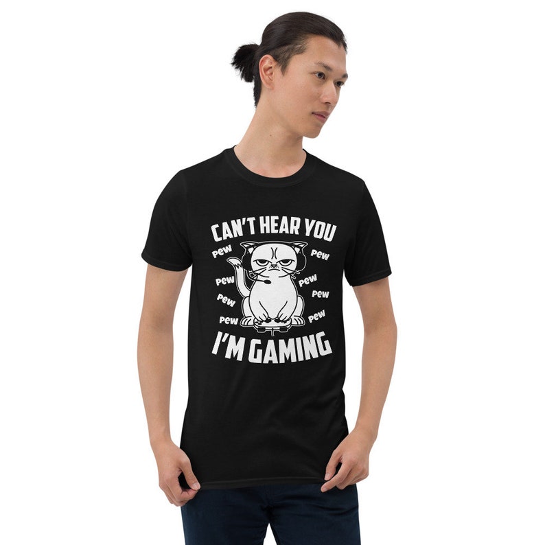 May include: A black t-shirt with a white graphic of a cat wearing headphones and holding a video game controller. The text "Can't hear you I'm gaming" is printed on the shirt, surrounded by the word "pew" repeated multiple times.