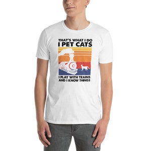May include: White t-shirt with a retro-style graphic of a train and a cat. The text on the shirt reads "That's what I do I pet cats I play with trains and I know things."