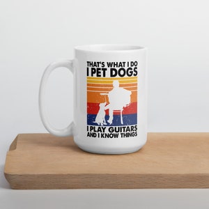 Puede incluir: Taza de caf&eacute; de cer&aacute;mica blanca con un dise&ntilde;o de estilo retro. La taza presenta una silueta de una persona tocando una guitarra con un perro sentado a su lado. El texto en la taza dice "That's what I do I pet dogs I play guitars and I know things."