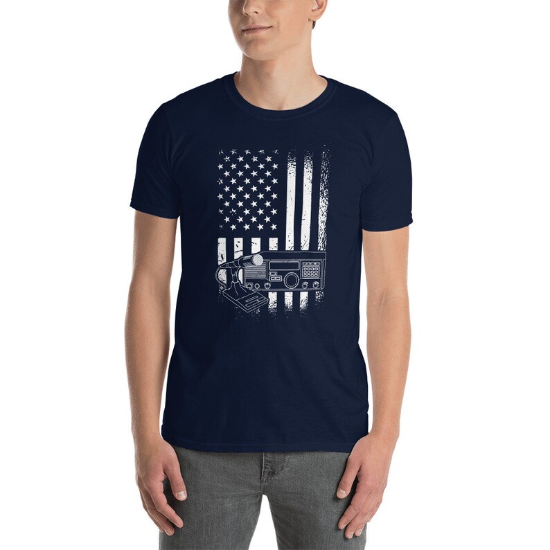 May include: A navy blue t-shirt with a white distressed American flag design. The flag has a radio transceiver in front of it.