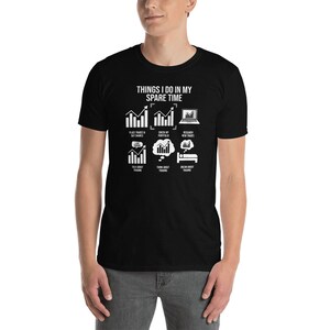 May include: Black t-shirt with white text that reads "Things I do in my spare time". The text is surrounded by icons depicting activities related to stock trading, such as placing trades, checking a portfolio, and researching new trades.