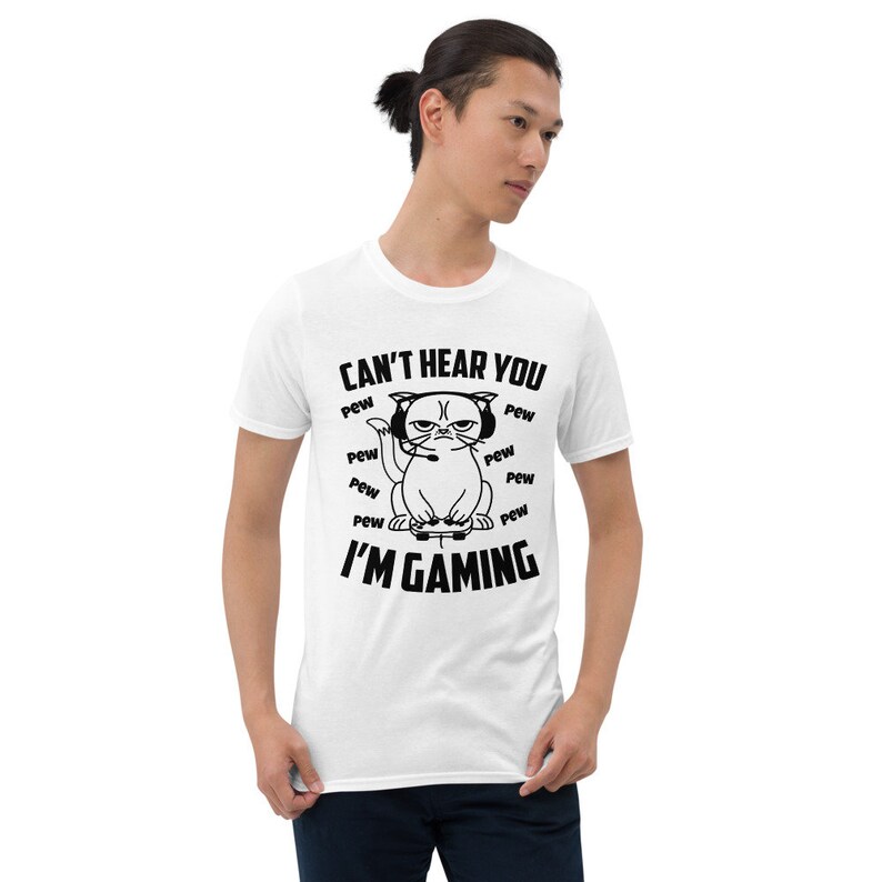 May include: White t-shirt with a black and white illustration of a cat wearing headphones and holding a video game controller. The text "CAN'T HEAR YOU" and "I'M GAMING" is printed on the shirt.