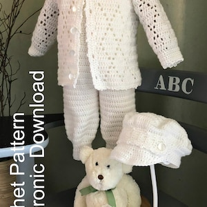 May include: White crocheted baby outfit with a cardigan, pants, hat, and booties. The outfit is displayed on a mannequin and a teddy bear. The text "Crochet Pattern Electronic Download" is visible on the left side of the image.