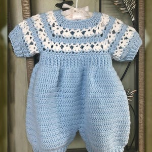 May include: A light blue crocheted baby onesie with white crocheted trim around the neckline and sleeves.