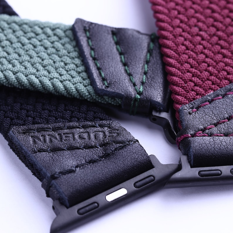 May include: Three different Apple Watch bands with black leather accents. The bands are green, black, and burgundy. The bands are made of woven nylon and have the word "Ninefold" embossed on the black band.