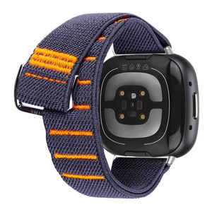 Puede incluir: Una banda de reloj el&aacute;stica gris y naranja con un reloj inteligente negro. El reloj inteligente tiene un sensor de frecuencia card&iacute;aca y una clasificaci&oacute;n de resistencia al agua de 5 ATM.