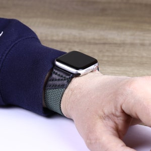 May include: A black and green woven watch band with a silver Apple Watch.