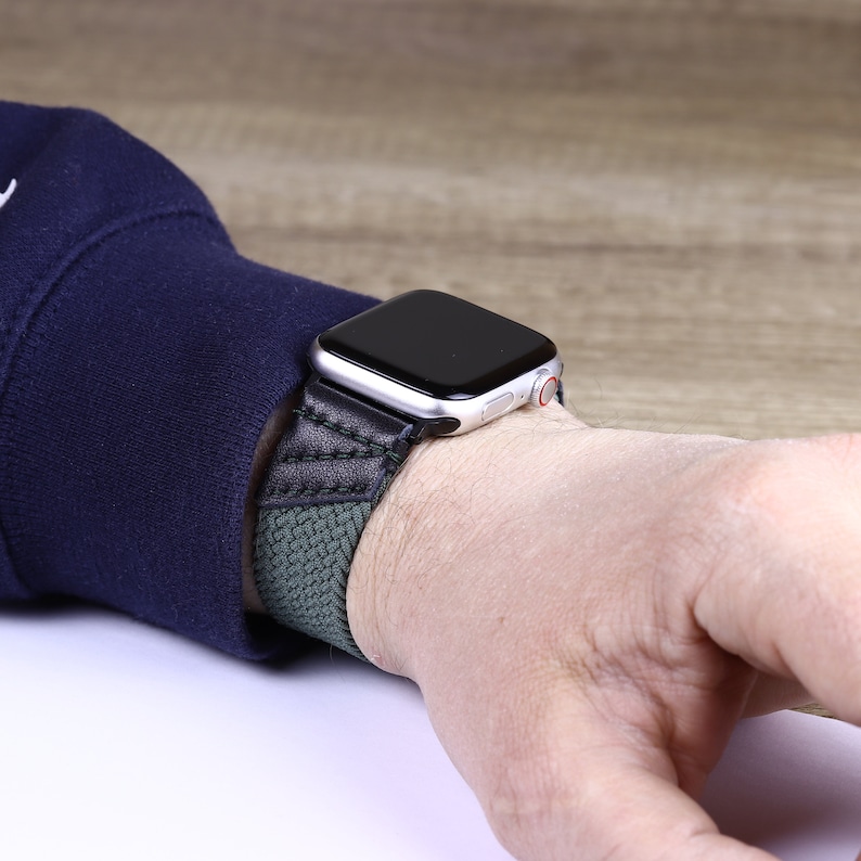 May include: A black and green woven watch band with a silver Apple Watch.