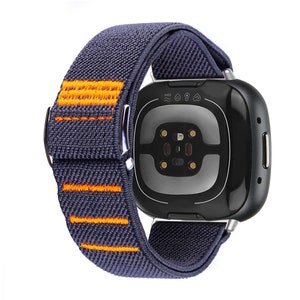 Puede incluir: Una correa de reloj el&aacute;stica de color gris oscuro y naranja con un reloj inteligente negro y plateado. La esfera del reloj tiene un sensor de frecuencia card&iacute;aca y el texto "5ATM" en la parte superior.