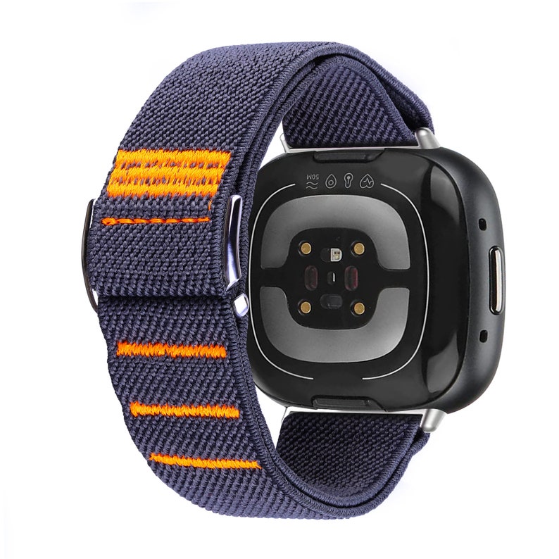 Puede incluir: Una correa de reloj el&aacute;stica de color gris oscuro y naranja con un reloj inteligente negro y plateado. La esfera del reloj tiene un sensor de frecuencia card&iacute;aca y el texto "5ATM" en la parte superior.