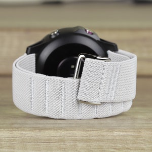 May include: A gray elastic watch band with a silver buckle. The band is attached to a black smartwatch with two small buttons on the side.