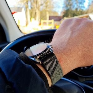 May include: A silver watch with a black leather band and a green fabric strap. The watch face is visible and has a silver bezel.