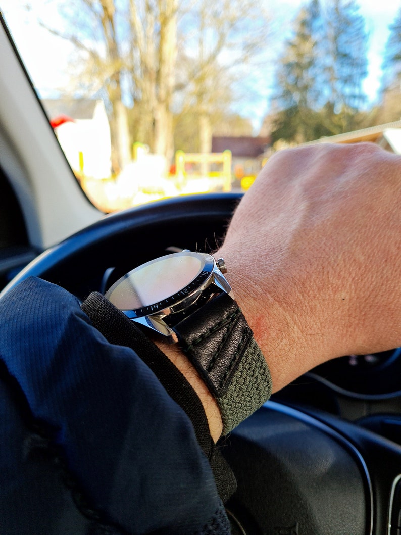 May include: A silver watch with a black leather band and a green fabric strap. The watch face is visible and has a silver bezel.
