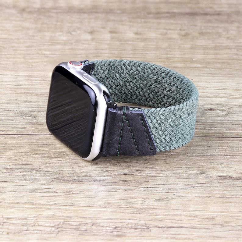 May include: A green and black braided watch band with a silver Apple Watch.