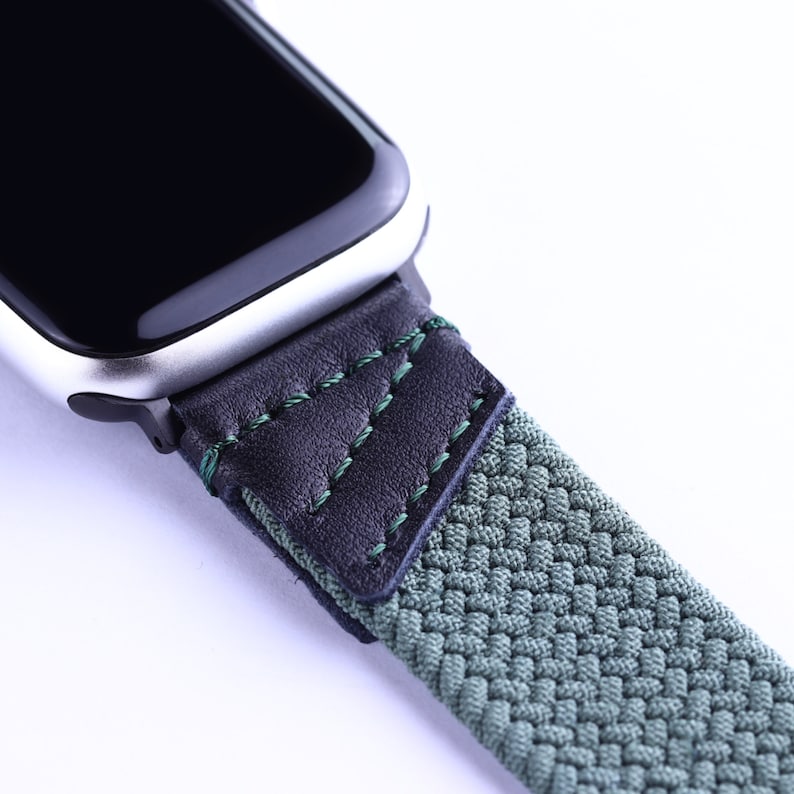 May include: A close-up of a green and black watch band with a braided fabric strap and a black leather section with green stitching.