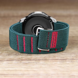 Op de afbeelding: Een groen en rood gestreept elastisch horlogebandje met een zilveren gesp. Het bandje is ontworpen voor een smartwatch.