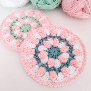 May include: Two crocheted doilies in pink, white, and teal. The doilies are circular and have a floral design.