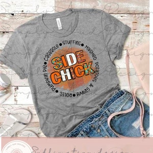 K&ouml;nnte beinhalten: Ein meliertes graues T-Shirt mit einem kreisf&ouml;rmigen Grafikdesign, das "SIDE CHICK" in Orange und Wei&szlig; zeigt, umgeben von den W&ouml;rtern "Pumpkin Pie", "Casserole", "Stuffing", "Mashed Potatoes", "Rolls" und "Gravy". Das Shirt wird mit Jeansshorts kombiniert.